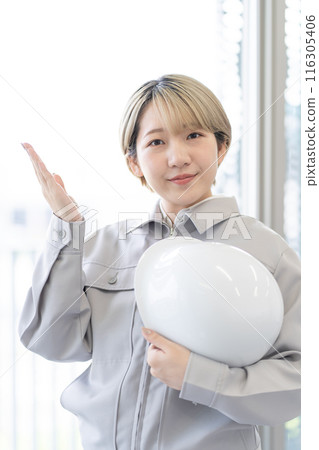 A young woman with short blonde hair wearing work clothes and holding a helmet (OK, free hair color, work the way you want, work environment) 116305406