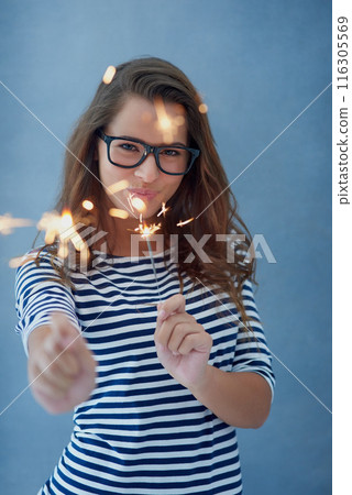 Woman, smile and portrait in studio with sparklers for celebration isolated on blue background with light. Confidence, glasses and fun event with birthday or new year with glow, vision and fireworks. Woman, smile and portrait in studio with sparklers for celebration isolated on blue background with light. Confidence, glasses and fun event with birthday or new year with glow, vision and fireworks. 116305569