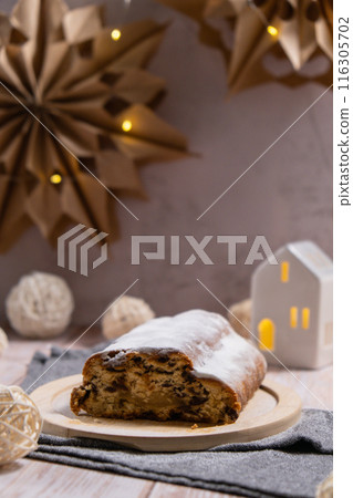 Christmas Stollen in Christmas lights and decoration. Traditional sweet fruit loaf with icing sugar festive pastry dessert. Holiday baking food Christmas Stollen in Christmas lights and decoration. Traditional sweet fruit loaf with icing sugar festive pastry dessert. Holiday baking food 116305702