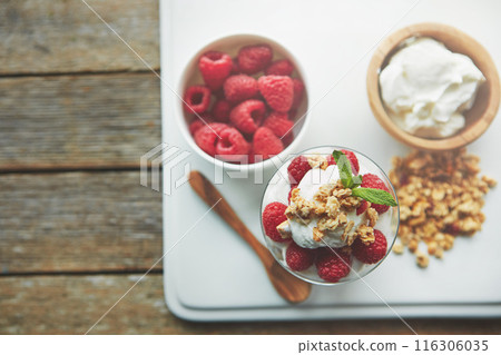 Yogurt, bowl and glass with raspberry in cereal for breakfast food, nutrition and snack in morning. Top view, fruit and dairy in container with wooden spoon for healthy meal, organic and vegan diet Yogurt, bowl and glass with raspberry in cereal for breakfast food, nutrition and snack in morning. Top view, fruit and dairy in container with wooden spoon for healthy meal, organic and vegan diet 116306035