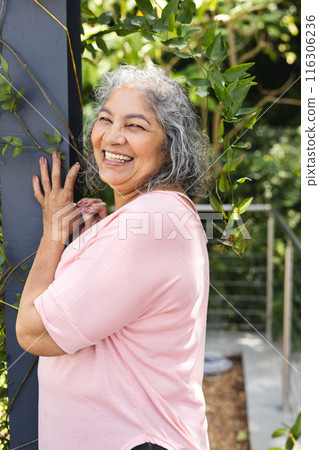 Senior biracial woman leaning against post, smiling outdoors 116306236