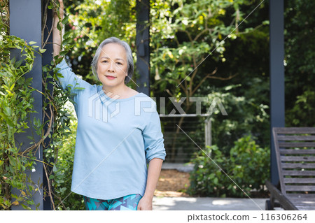 Outdoors, senior Asian woman leans on a garden post, copy space 116306264