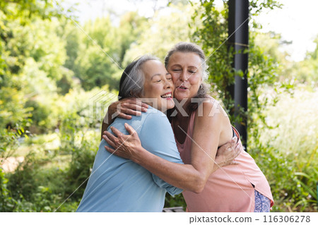Outdoors, diverse senior female friends hugging, wearing casual clothes 116306278