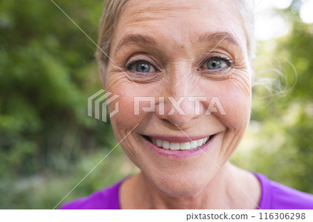 Outdoors, senior Caucasian female wearing a purple top, smiling at camera 116306298