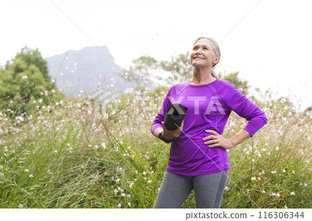 Outdoors, Caucasian senior female holding a yoga mat in a field, copy space 116306344