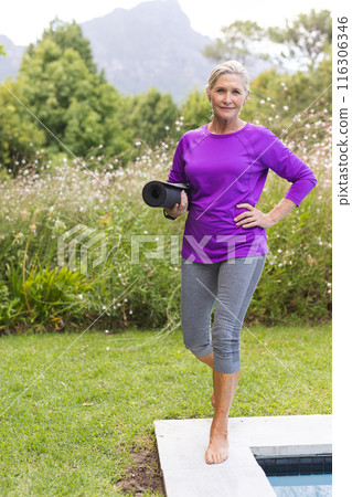 Outdoors, Caucasian senior female holding a yoga mat by a pool 116306346