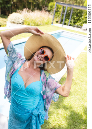Outdoors, Caucasian senior female relaxing poolside, donning a large hat Outdoors, Caucasian senior female relaxing poolside, donning a large hat 116306355