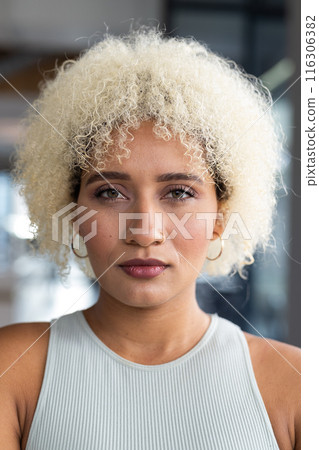 In modern office, biracial young woman with curly blonde hair standing alone 116306382