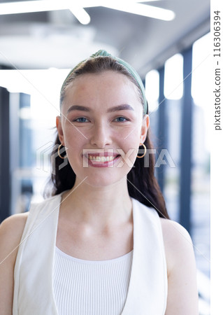 In modern office, Caucasian young woman wearing white top, smiling at camera 116306394