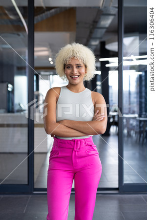 In modern office, young biracial woman standing, smiling at camera In modern office, young biracial woman standing, smiling at camera 116306404