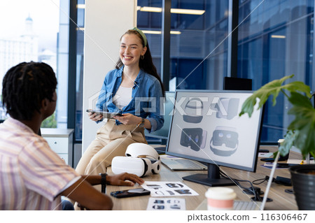 Diverse young team in casual clothes discusses over a tablet in a modern office Diverse young team in casual clothes discusses over a tablet in a modern office 116306467
