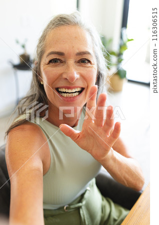 At home, mature Caucasian woman waving and smiling during video call 116306515