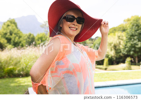 Senior Asian woman wearing sunglasses relaxing outdoors by pool 116306573