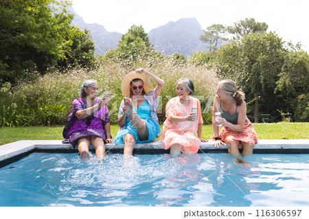 Outdoors, diverse senior female friends gathering by pool, laughing 116306597