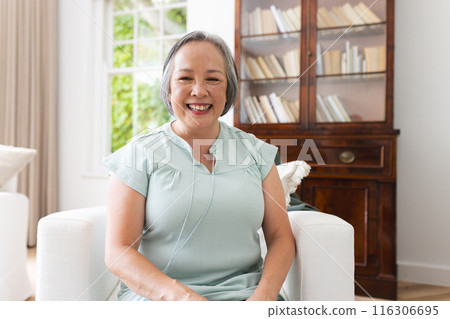 Senior Asian woman sitting at home during video call, smiling in a bright room Senior Asian woman sitting at home during video call, smiling in a bright room 116306695