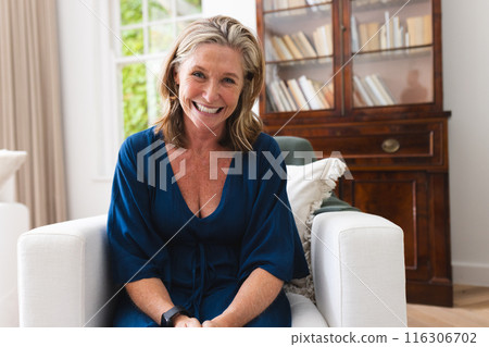 Caucasian senior woman in blue dress enjoying video call at home, smiling 116306702