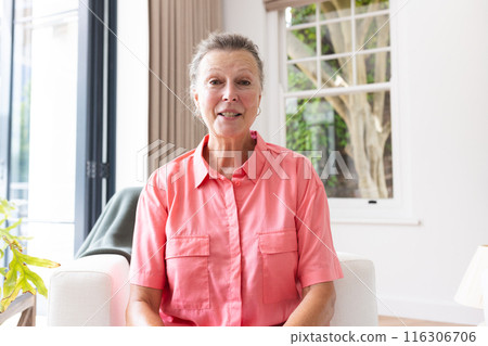 Caucasian senior woman wearing pink shirt, smiling during video call at home 116306706