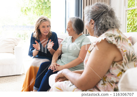Diverse senior female friends chatting at home, lounging on sofa 116306707