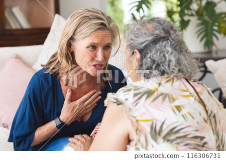 Diverse senior female friends discussing at home, showing concern 116306731