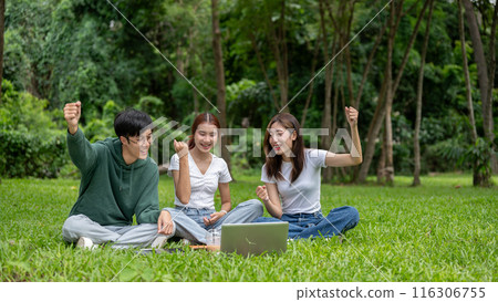 Cheerful students is checking their exam scores on a laptop and celebrating together in a park. 116306755