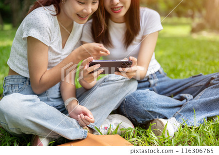 Two lovely Asian female friends are enjoying talking and watching something on a smartphone. Two lovely Asian female friends are enjoying talking and watching something on a smartphone. 116306765