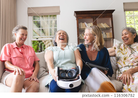 Diverse senior female friends laughing together on couch at home Diverse senior female friends laughing together on couch at home 116306782