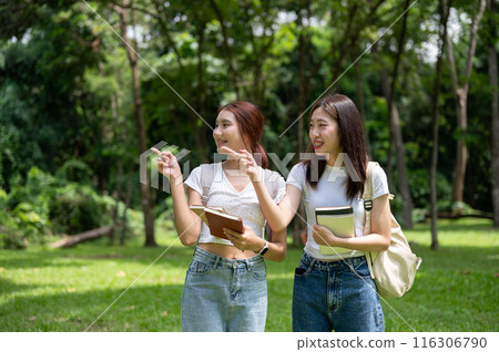 Two happy young Asian female college students with backpacks are walking in the park together. 116306790
