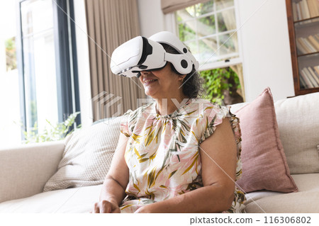 Senior biracial woman wearing virtual reality headset at home, sitting on couch Senior biracial woman wearing virtual reality headset at home, sitting on couch 116306802