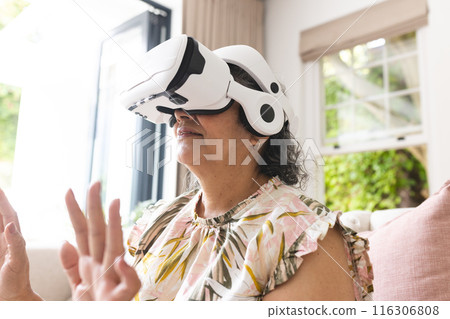 A senior biracial woman wearing VR headset sits on couch at home A senior biracial woman wearing VR headset sits on couch at home 116306808