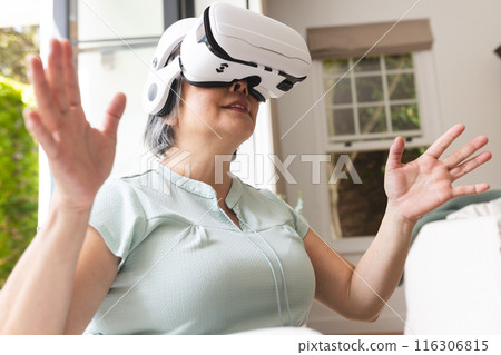 Senior Asian woman at home uses VR headset to explore a digital world Senior Asian woman at home uses VR headset to explore a digital world 116306815