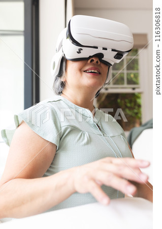 Asian senior female wearing virtual reality headset, sitting at home Asian senior female wearing virtual reality headset, sitting at home 116306818