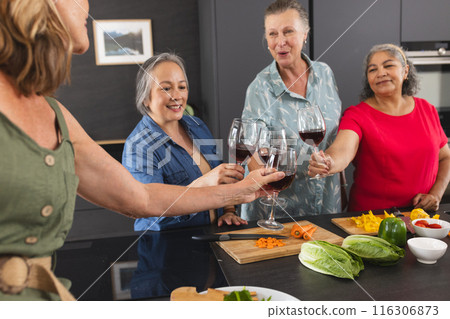 Diverse senior female friends enjoying wine at home in kitchen Diverse senior female friends enjoying wine at home in kitchen 116306873
