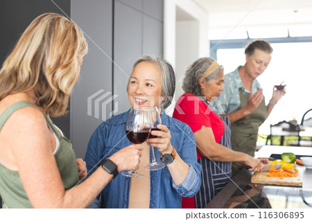 Diverse senior female friends gathering in kitchen at home, chatting and cooking 116306895