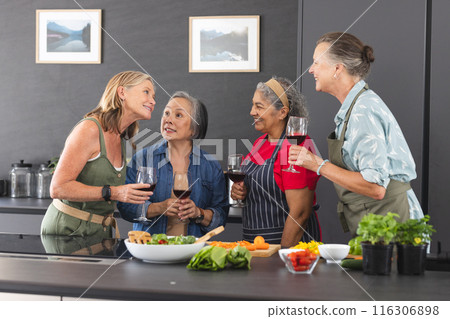 Diverse senior female friends are enjoying wine at home in cozy kitchen Diverse senior female friends are enjoying wine at home in cozy kitchen 116306898