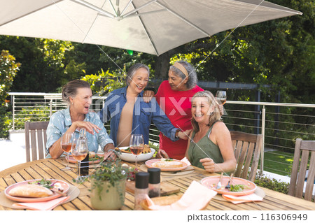 Diverse senior female friends enjoying lunch outdoors under umbrella Diverse senior female friends enjoying lunch outdoors under umbrella 116306949
