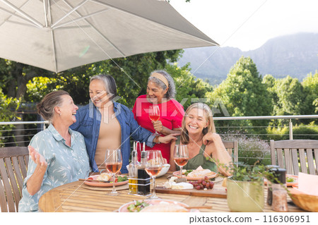 Diverse senior female friends laughing over outdoor meal Diverse senior female friends laughing over outdoor meal 116306951
