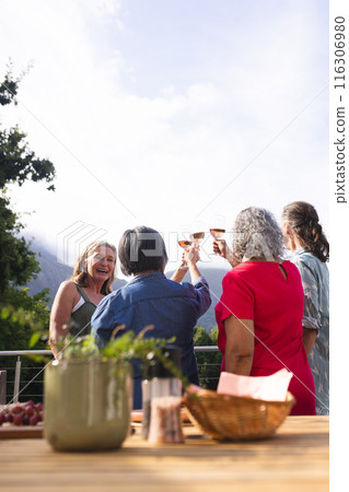Diverse senior female friends laughing over drinks outside 116306980