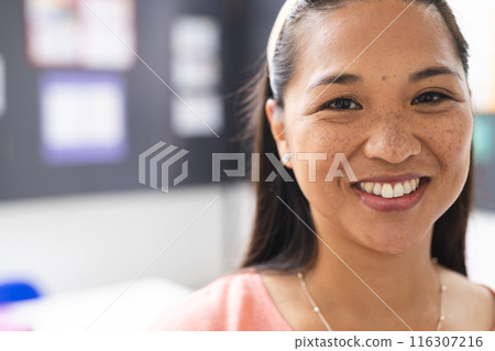 A young biracial female teacher in classroom smiles at camera with copy space 116307216