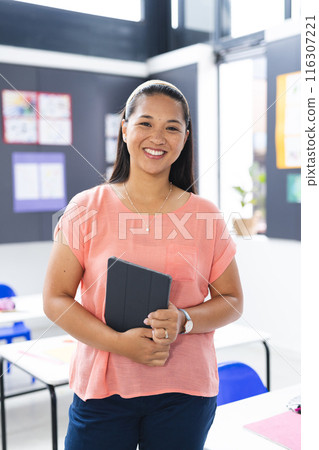 In school, young biracial female teacher holding a tablet in the classroom 116307221