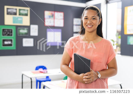 In school, in classroom, biracial young female teacher holding a tablet smiles with copy space 116307223