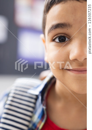 In school, young biracial boy with a striped shirt is smiling in the classroom, copy space In school, young biracial boy with a striped shirt is smiling in the classroom, copy space 116307235