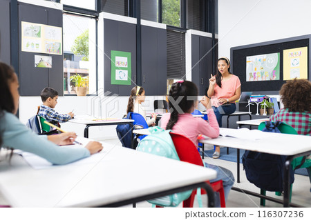 In school, in a classroom, a young biracial female teacher is explaining a lesson In school, in a classroom, a young biracial female teacher is explaining a lesson 116307236