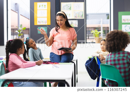 In school, in the classroom, a young biracial female teacher is explaining to her diverse students In school, in the classroom, a young biracial female teacher is explaining to her diverse students 116307245