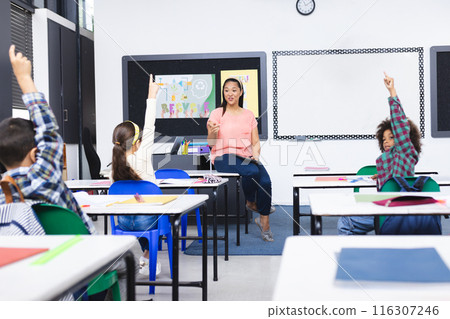 In school, young biracial female teacher explaining in classroom, students raising hands 116307246