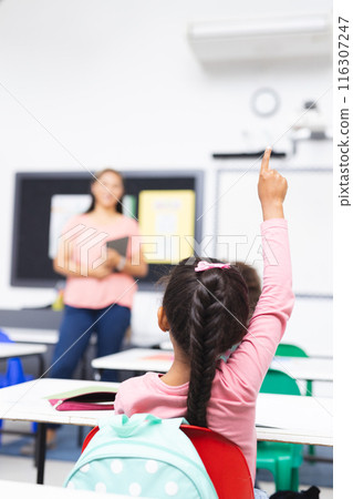 A biracial female teacher holds tablet, student raises her hand, copy space 116307247