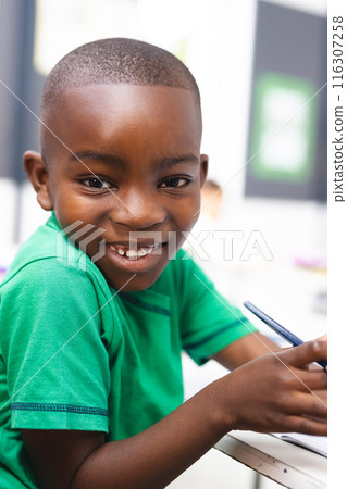 In school, young African American boy wearing a green shirt is writing in the classroom In school, young African American boy wearing a green shirt is writing in the classroom 116307258
