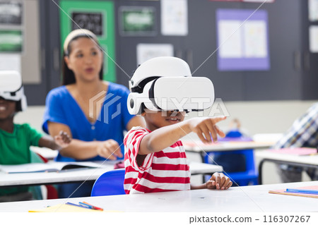 In school, in classroom, biracial female teacher watches students wearing VR headsets 116307267