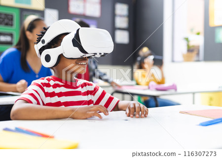 In school, young African American boy wearing a VR headset sits at a desk in the classroom, copy spa 116307273
