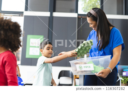 In school, in the classroom, a diverse teacher is showing recycling to two young students 116307282