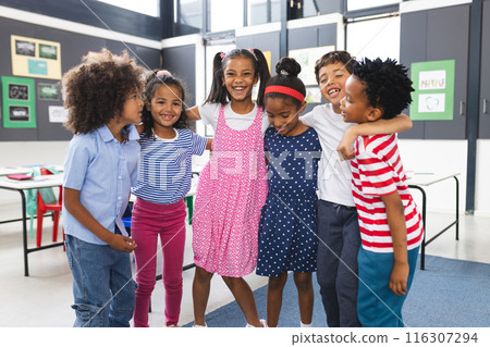 In school, diverse group of young students is hugging and laughing together in the classroom 116307294